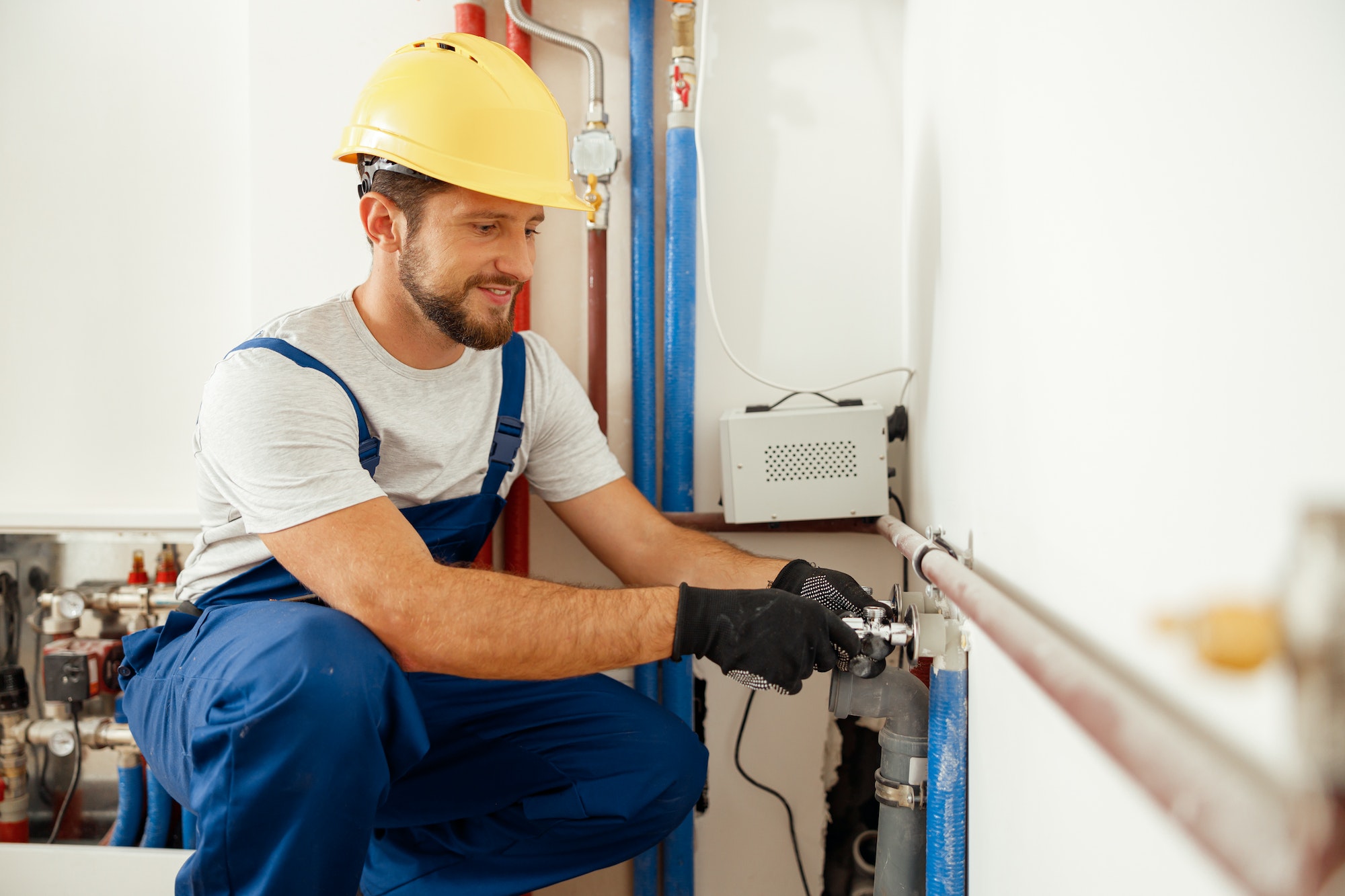 Cheerful male worker, plumber checking pipes while installing heating system in apartment
