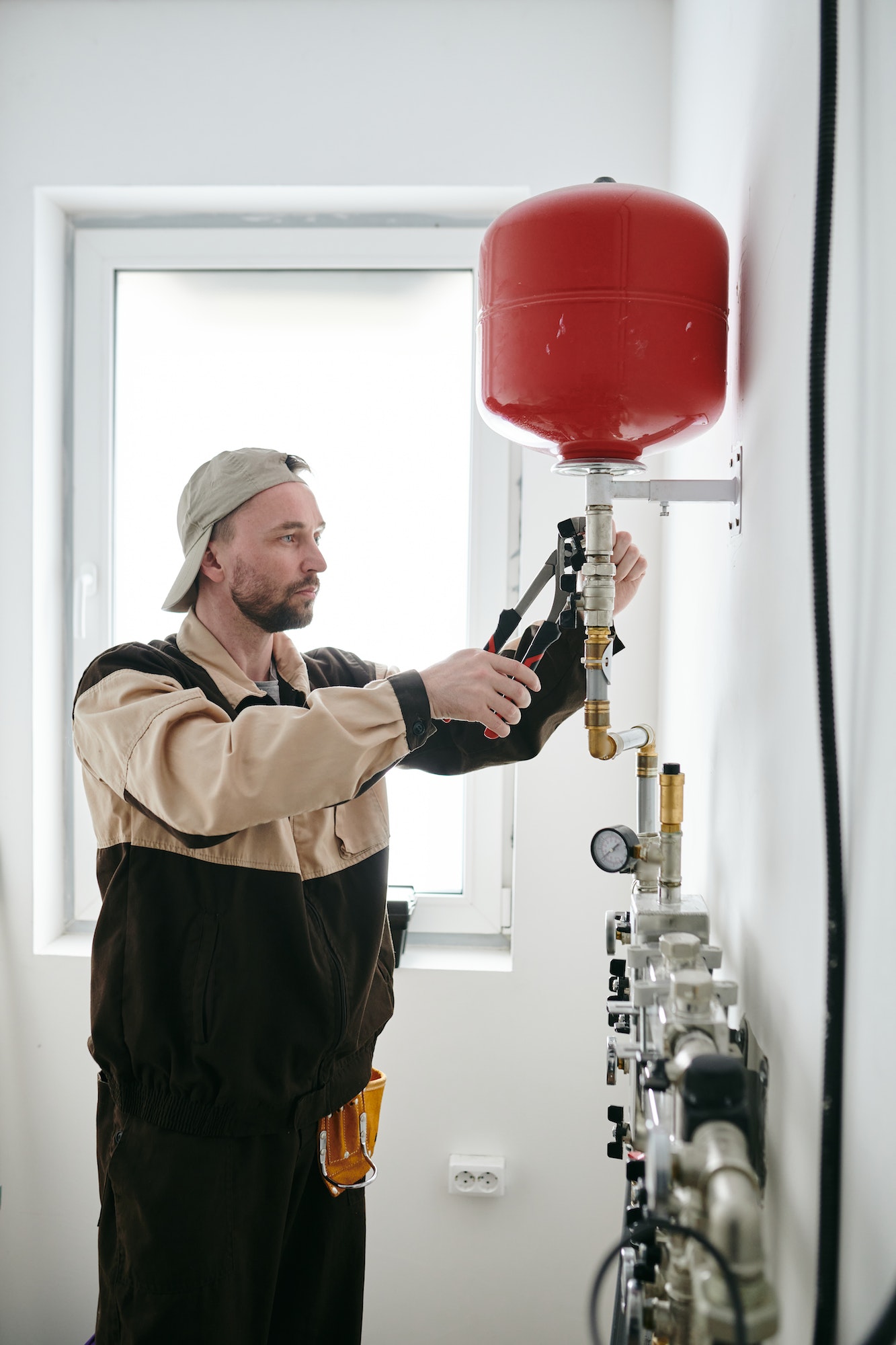 Repairman in uniform fixing part of pipe in new apartment